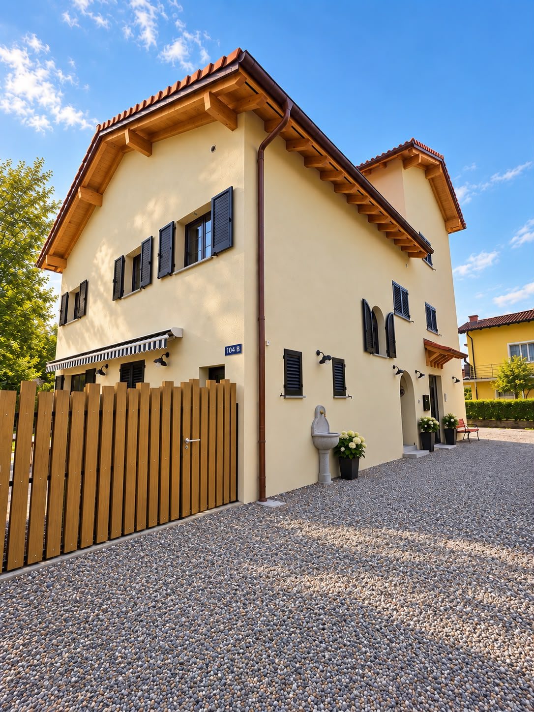 La casa del B&B Airone a Coldrerio nella luce del pomeriggio: facciata chiara, persiane scure, la staccionata di legno e il numero 104 B