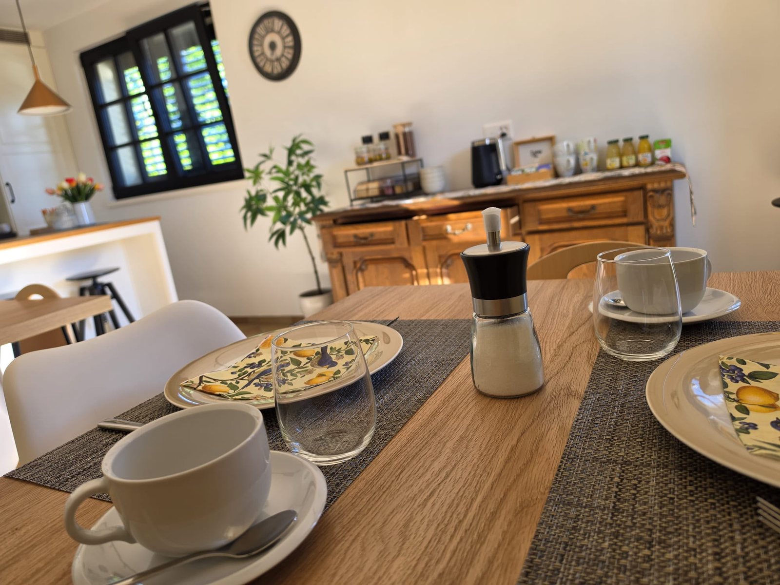 La tavola della colazione apparecchiata, con le tazze e i tovaglioli ai limoni, e la credenza del buffet sullo sfondo
