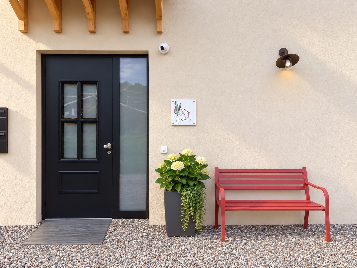 L’ingresso del B&B Airone: la porta scura, la panchina rossa, le ortensie e l’insegna con l’airone